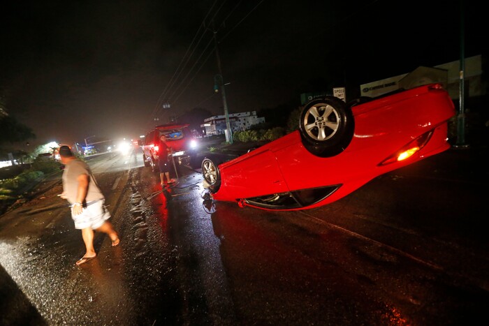 People tend to a car that flipped over on Cape Coral Parkway during Hurricane Irma, in Cape Coral, Fla., Sunday, Sept. 10, 2017. (AP Photo/Gerald Herbert)
