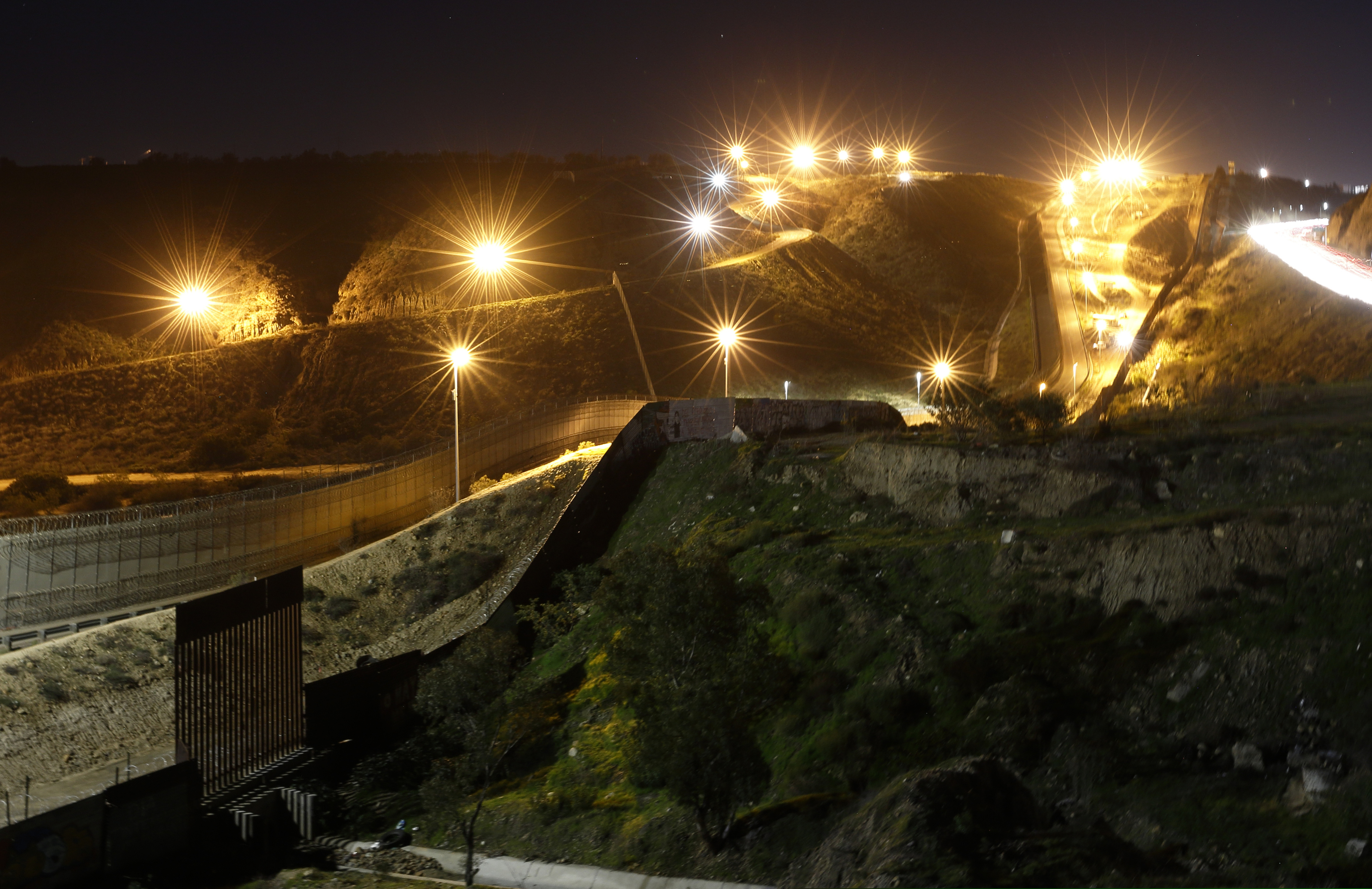(Gregory Bull | The Associated Press) In this Monday, Jan. 7, 2019, file photo, floodlights from the U.S, illuminate multiple border walls, seen from Tijuana, Mexico. The migrant caravan that was seized upon by U.S. President Donald Trump in the run-up to the 2018 election has quietly dwindled to a few hundred people, with many of them having crossed into the U.S. or put down roots in Mexico.