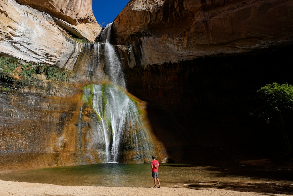 FILE - A hiker watches a waterfall at Lower Calf Creek Falls at Grand Staircase Escalante National Monument Wednesday, July 12, 2023, in Escalante, Utah. A federal judge Friday, Aug. 11, 2023 dismissed a lawsuit from the state of Utah and two rural counties that challenged President Joe Biden's restoration of two sprawling national monuments that former President Donald Trump had downsized. (AP Photo/Ross D. Franklin, File)