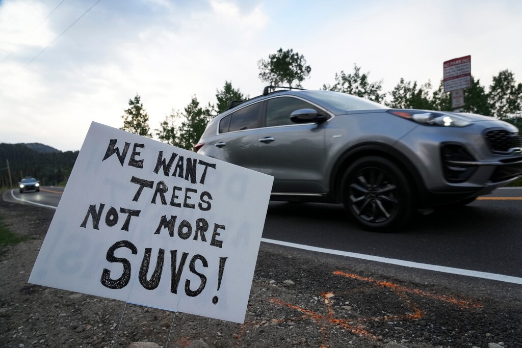 (Bethany Baker | The Salt Lake Tribune) Cars drive past a sign, seen here along South Guardsman Pass Road near Brighton on Tuesday, July 15, 2025, that opposes the requested 593-space parking lot for Solitude Mountain Resort that would be in an aspen grove across SR-190 from the ski area's main village. The lot would require steep retaining walls and the removal of hundreds of trees, could also damage Salt Lake City's watershed, further snarl traffic in the canyon and be a visual blight.