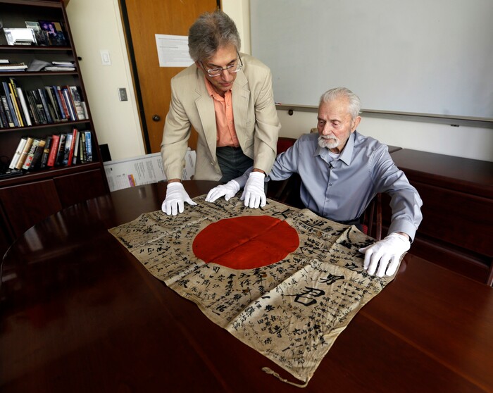 In this Monday, Aug. 7, 2017 photo, WWII veteran Marvin Strombo, right, and Obon Society executives director Rex Zika lay out a Japanese flag with names written on it in Portland, Ore. Strombo recovered the flag from a dead Japanese soldier in the Pacific more than 70 years ago and now, at age 93, will return the flag to the Japanese man's surviving siblings. (AP Photo/Don Ryan)