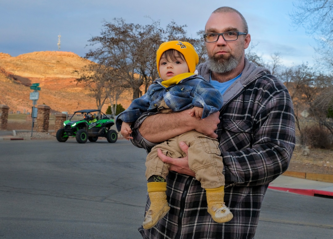 (Leah Hogsten | The Salt Lake Tribune) Moab native Anthony Charles, holding his son, Winter, 9 months, struggles with the noise of off-road utility terrain vehicles (UTVs) since he and his wife moved into their new home on Mill Creek Drive in May 2020. Charles and Winter stand at the 3 road intersection of Mill Creek Drive and Sand Flats Road, which leads to the Sand Flats Recreation Area from Moab, Feb. 19, 2021. Charles has said he has counted over 70 UTVs at that intersection when several groups converged one day at the three-way stop.