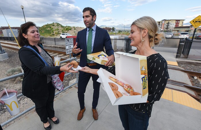 (Francisco Kjolseth | The Salt Lake Tribune) In honor of National Donut Day, Sandy Mayor Kurt Bradburn, center, teams up with Deputy Mayor Evelyn Everton, right, and the Sandy Police Department as morning commuter Pepper Poulsen takes them up on their offer on Friday, June 1, 2018, at the Sandy Civic Center TRAX Station.