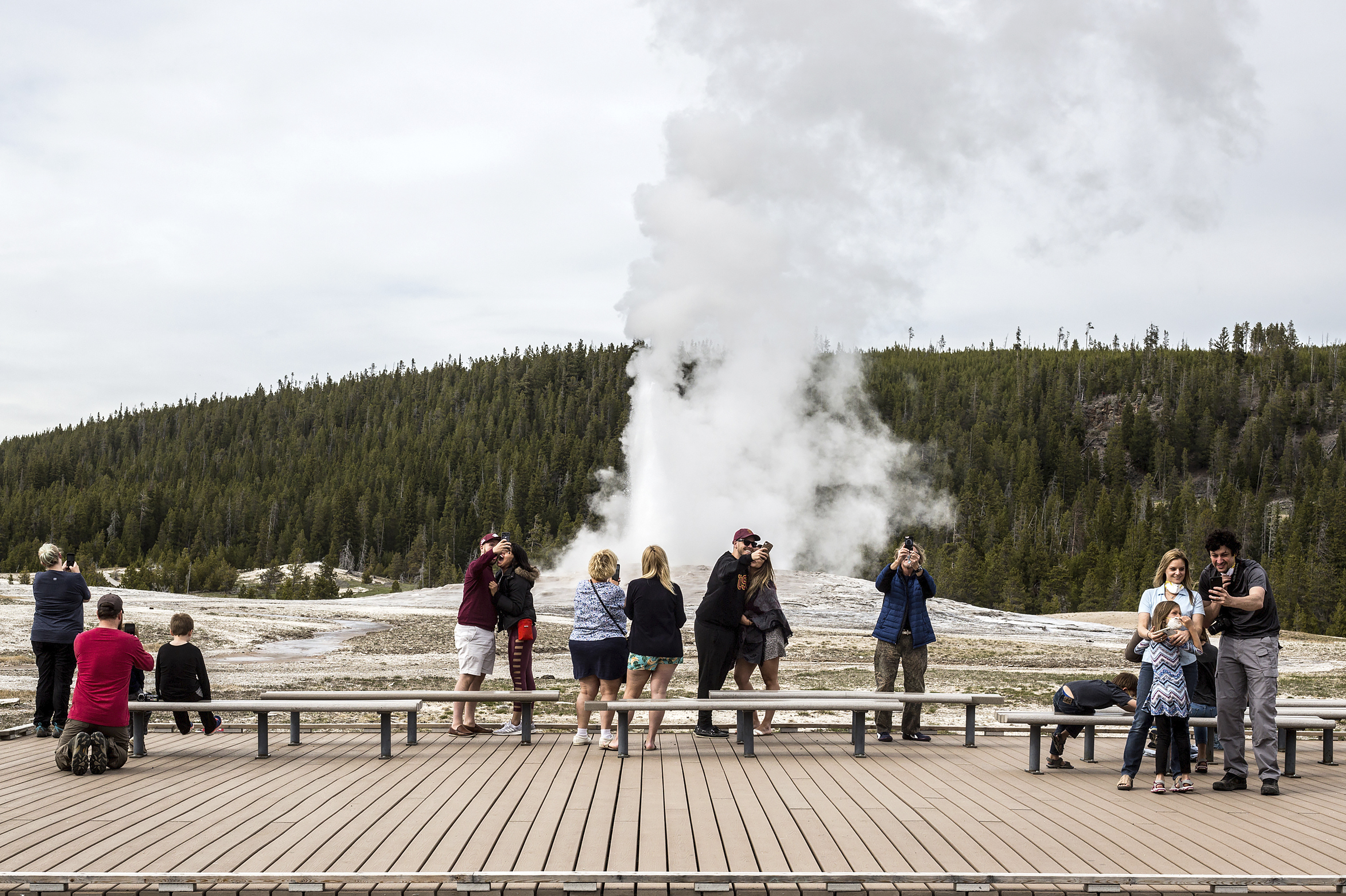 (Ryan Dorgan | Jackson Hole News & Guide via AP) In this Monday, May 18, 2020 photo, visitors watch as Old Faithful erupts on the day the park partially reopened after a two-month shutdown due to the coronavirus pandemic, at Yellowstone National Park, Wyo. Officials at Yellowstone and other national parks plan to let tourists mostly police themselves and not intervene much to enforce social distancing.