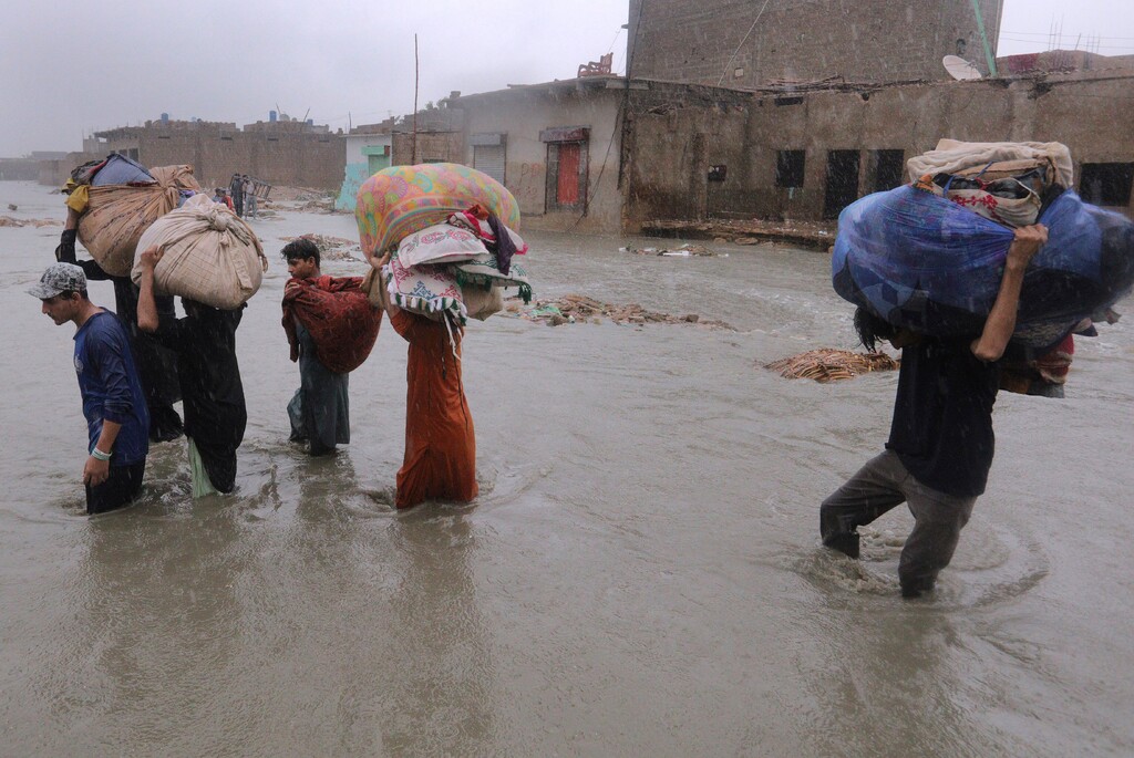 Fareed Khan | AP ) Residents carry salvaged belongings as they wade through a flooded area during a heavy monsoon rain in Yar Mohammad village near Karachi, Pakistan, Thursday, Aug. 27, 2020.