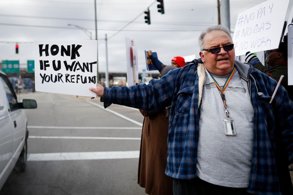 (John Minchillo | The Associated Press) In this Jan. 10, 2019, photo, Will Kohler, an IRS tax examiner, holds a protest sign as union members and other federal employees rally to call for an end to the partial government shutdown outside the IRS site, in Covington, Ky. Kohler applied for unemployment after getting furloughed but said his application is in limbo because the Treasury Department office that needs to verify his claim is closed as a result of the shutdown.