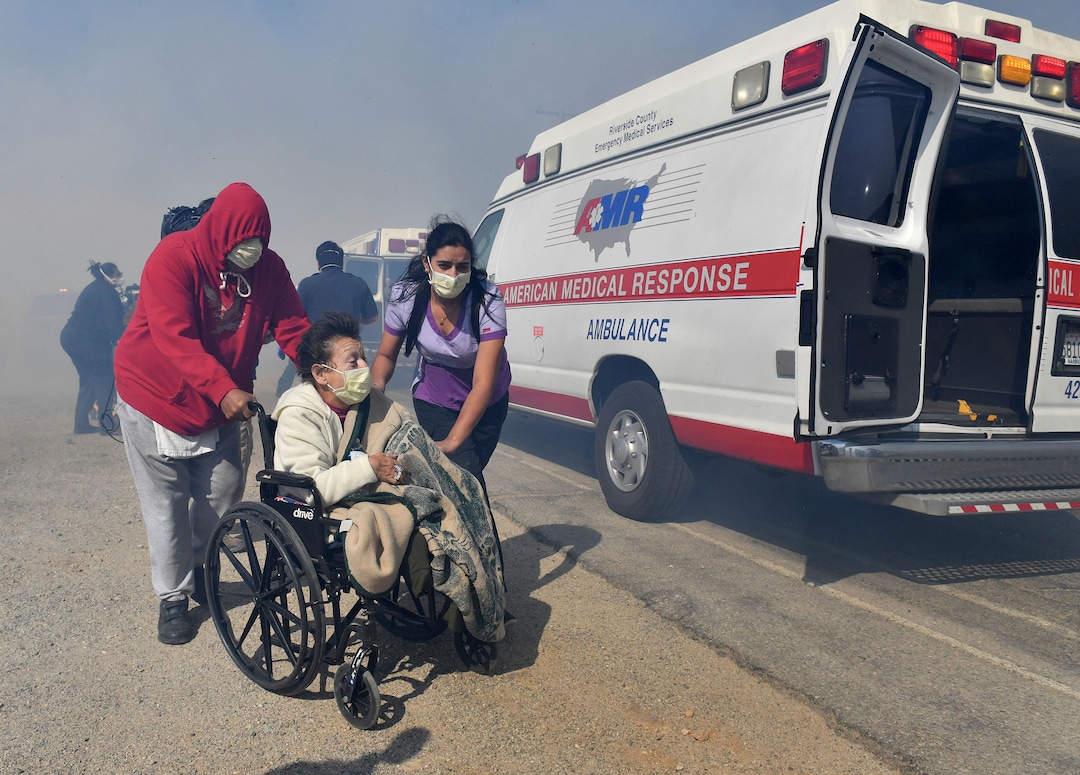 (Will Lester | The Orange County Register via AP) Elderly residents of the Riverside Heights Healthcare Center in Jurupa Valley, Calif., are evacuated from their care facility as flames and smoke from the Hill Fire approach Wednesday Oct 30, 2019.