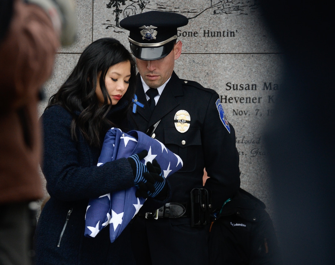 (Francisco Kjolseth  |  The Salt Lake Tribune)  Elizabeth Romrell is accompanied by South Salt Lake officer Lewis Lombardo as she holds the flags she was presented by the Marine Corps and South Salt Lake police department during funeral services for her husband, police officer David Romrell, at Larkin Sunset Gardens Cemetery in Sandy, Wed. Dec. 5, 2018.