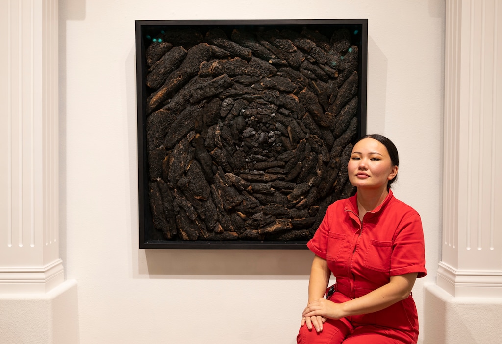 (Aziza Abdieva) Artist Aziza Abdieva sits next to one of her works featured in the exhibition "Fear Alchemy," now on display at the St. George Museum of Art.