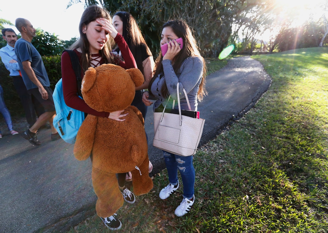 Students wait to be picked up after a shooting at Marjory Stoneman Douglas High School in Parkland, Fla., Wednesday, Feb. 14, 2018. A shooter opened fire at the Florida high school Wednesday, killing people, sending students running out into the streets and SWAT team members swarming in before authorities took the shooter into custody. (AP Photo/Wilfredo Lee)