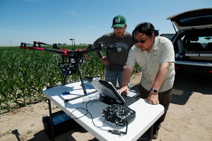 (David Zalubowski | AP Photo) In this Thursday, July 11, 2019, photograph, United States Department of Agriculture intern Alex Olsen, left, and engineering technician Kevin Yemoto work to set up a drone for flight over a research farm northeast of Greeley, Colo. Researchers are using drones carrying imaging cameras over the fields in conjunction with stationary sensors connected to the internet to chart the growth of crops in an effort to integrate new technology into the age-old skill of farming.